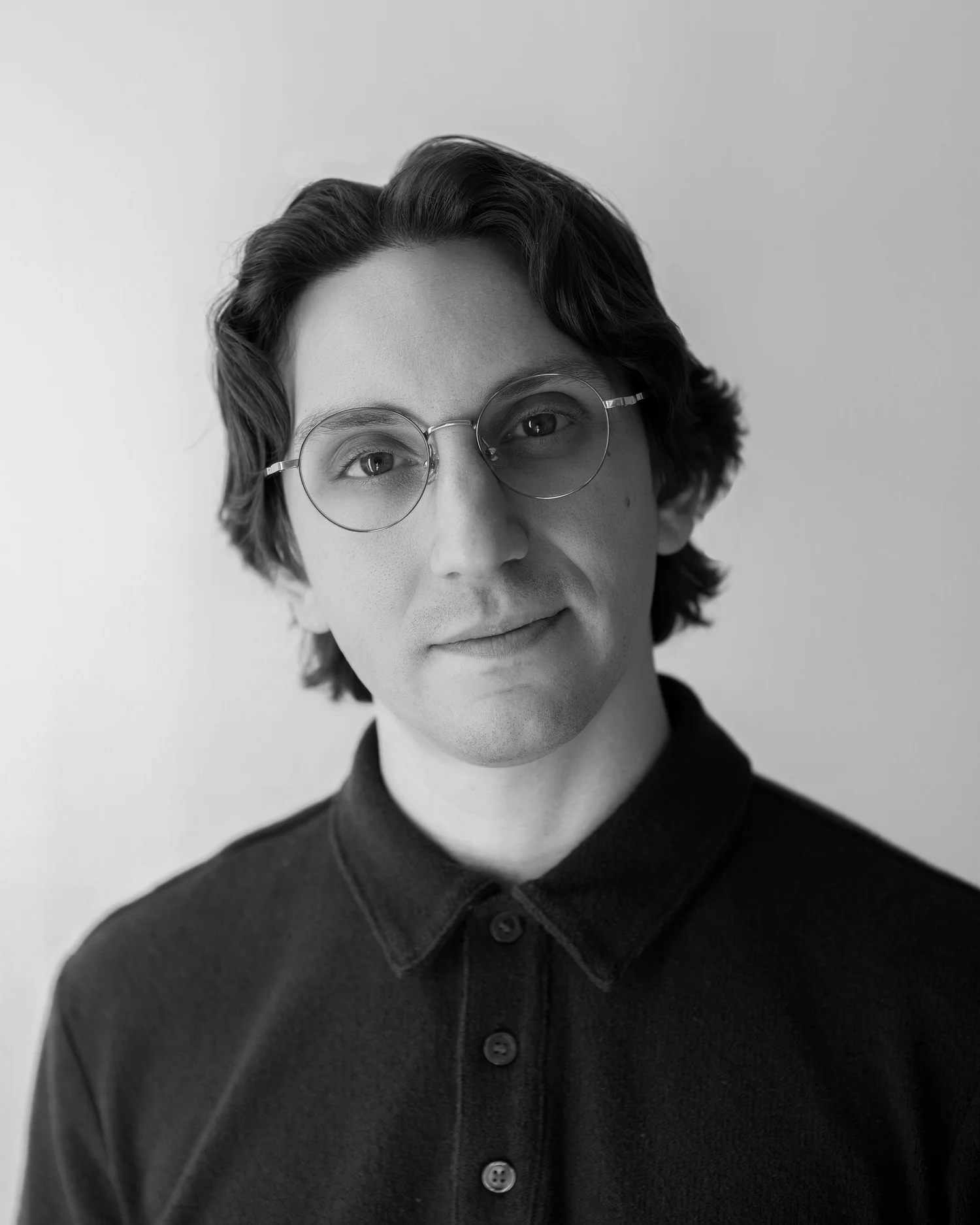 Black and white portrait of a young man with wavy hair, wearing round glasses and a collared shirt.